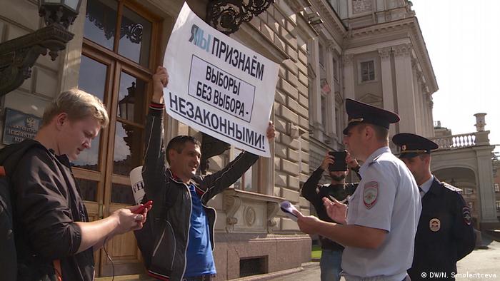 Человек с плакатом о непризнание выборов, перед ним два полицейских 