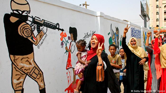 Sudanese celebrating the agreement between the military and civilian protesters in front of wall with graffitti depicting protests and a soldier (Getty Images/AFP/E. Hamid)