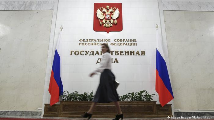 Девушка проходит мимо флагов России и барельефа на стене - герба России и надписи Государственная дума 