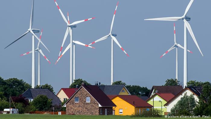 An assortment of houses standing against a backdrop of huge wind turbines