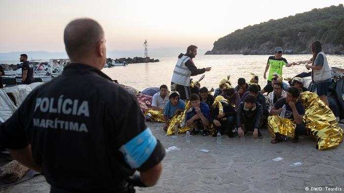 A policeman at the docks in Lesbos supervising a group of refugees