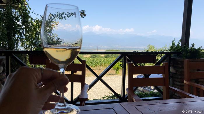 A glass of amber Georgian wine, a view of the vineyard in the background