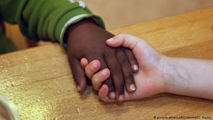 Mãos de duas crianças, durante aperto de mãos, uma negra, outra branca