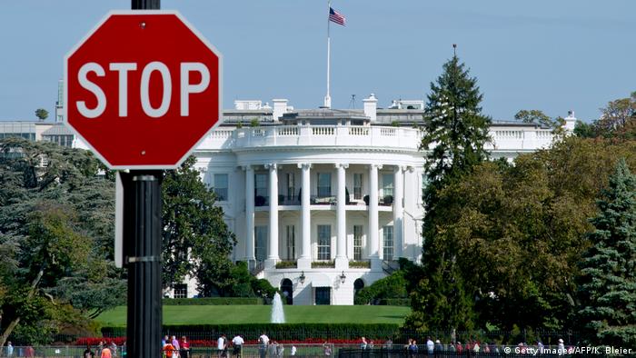 Красный знак с надписью Стоп на фоне Белого дома в Вашингтоне