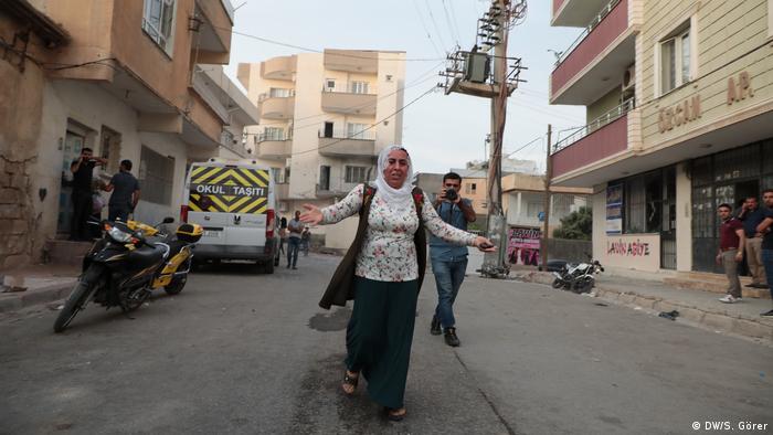 Mulher de véu corre de braços abertos em rua da Síria