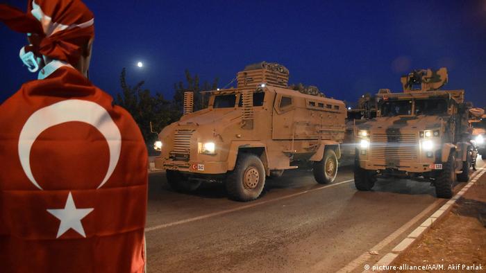 A Turkish convoy drives down the street at night while a person wrapped in a Turkish flag watches the convoy (picture-alliance/AA/M. Akif Parlak)
