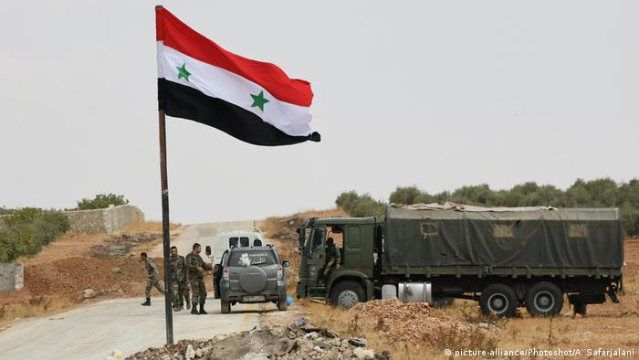 Bandeira síria em região árida com caminhão militar ao fundo