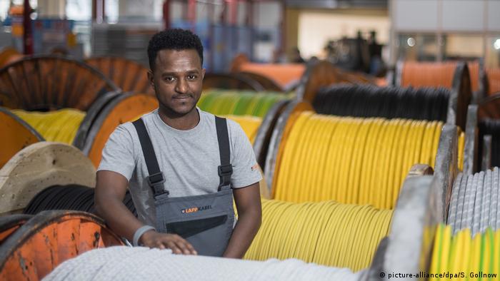 An Eritrean refugee stands between cable reels at the cable manufacturer Lapp in Germany