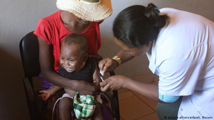 A woman holds a crying baby while a nurse gives a vaccination