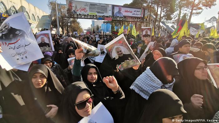 Multidão de mulheres vestidas de preto com véu islâmico levantando retratos de Soleimani