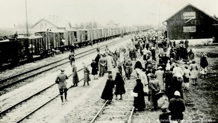 Photo of people standing beside railroad tracks in 1944, guarded by SS members (Holokauszt Emlékközpont, Budapest )
