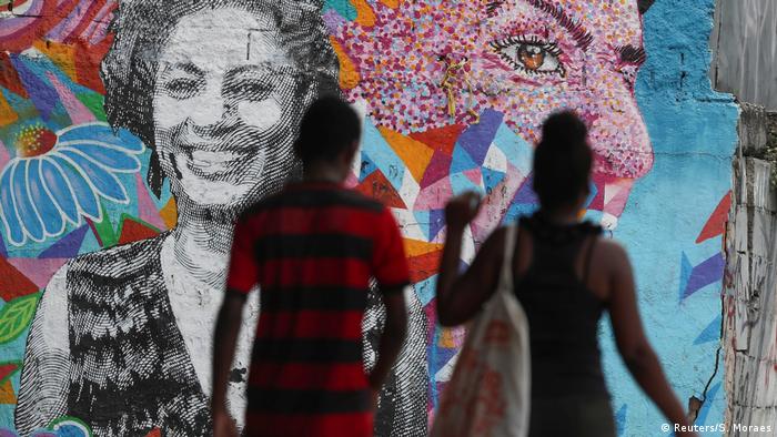 Casal passa na frente de um grafite com o rosto da vereadora Marielle Franco
