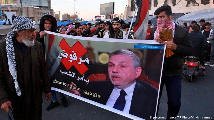 Protesters chant slogans while holding a poster of newly appointed Prime Minister Mohammed Allawi
