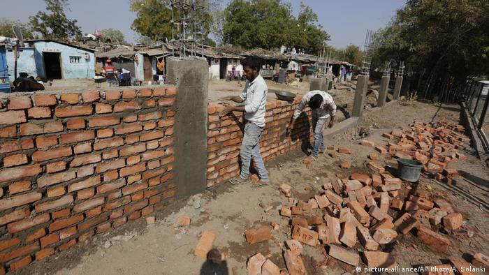 Bricklayers build a wall in front of slum (picture-alliance/AP Photo/A. Solanki)