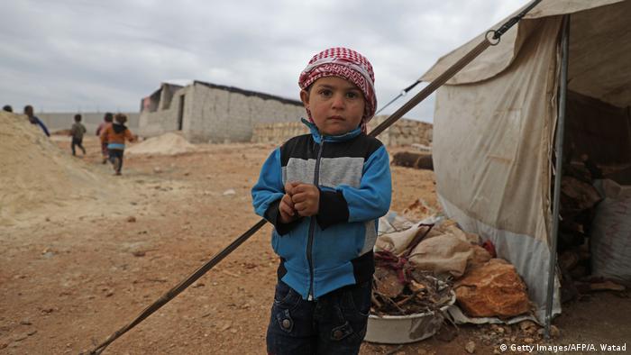 A Syrian boy stands outside a tent at an informal camp in Kafr Lusin village