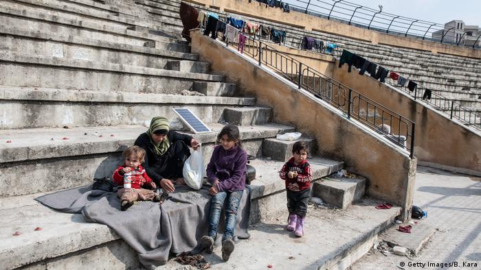 Displaced Syrians sit on the tribunes of a stadium which has been turned into a makeshift refugee shelter