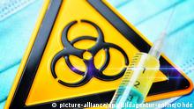 Symbolfoto Vorsichtsmaßnahmen Coronavirus | Spritze und Biogefährdungsschild auf Mundschutz