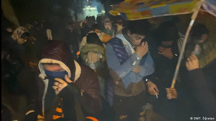 People shield their eyes from tear gas and smoke at night