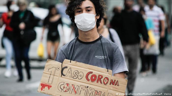 Jovem com máscara segura cartaz: Primeiro caso corona confirmado