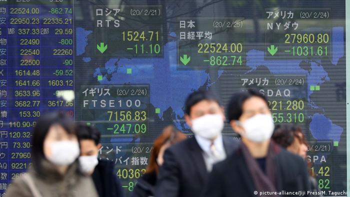 People walk in front of sign showing stock markets (picture-alliance/Jiji Press/M. Taguchi)