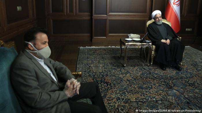 President Rouhani sits in a chair while a minister wears a mask (Imago-Images/ZUMA Wire/Iranian Presidency)
