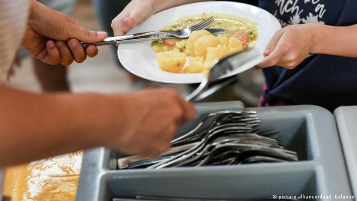 Посетители общественной столовой держат в руках тарелку с картофелем и овощами и столовые приборы.