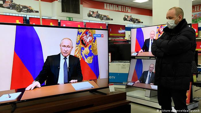 Мужчина в маске смотрит выступление Путина о коронавирусе по телевизору