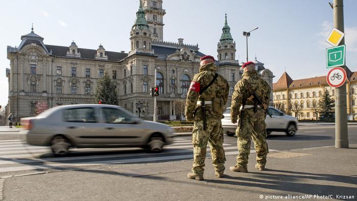 Military men stand on a street in Gyor, Hungary, as cars drive by (picture-alliance/AP Photo/C. Krizsan)