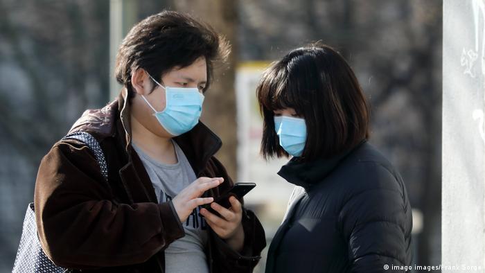 Two people wearing face masks look at a smartphone