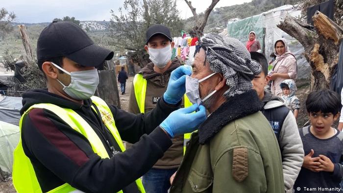 An aid worker fits a person with a face mask at the Moria refugee camp ( Team Humanity)