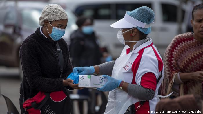 A woman wearing gloves and a mask hands out gloves to someone waiting in line for coronavirus testing
