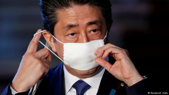 Japan's Prime Minister Shinzo Abe adjusts his face mask