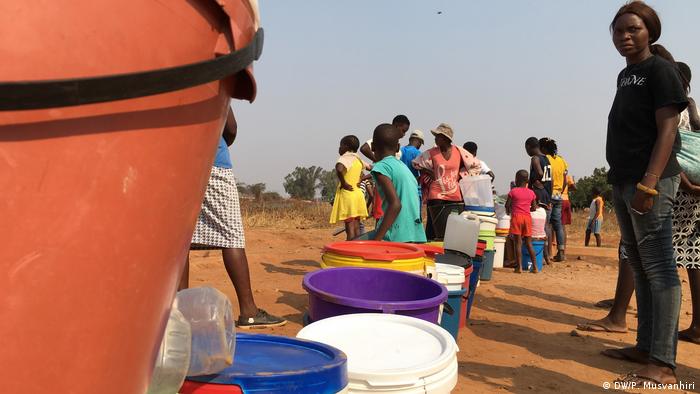 Fila de pessoas ao lado de baldes no Zimbábue. Pessoas esperam para encher recipientes com água potável