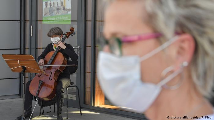 Fotoğrafta Almanya'daki maskeli bir kadın ve sokak müzisyeni görünüyor