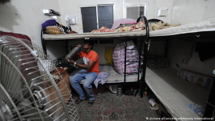 A migrant worker sits on a bed in a small room in a labor camp in Qatar (picture-alliance/dpa/Amnesty International)