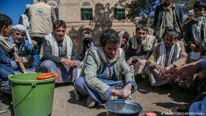 A man scrubs his hands near a pot of water (UNICEF/UNI324899/AlGhabri)