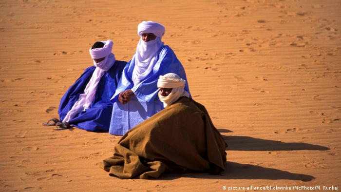 Drei Tuareg sitzen in langen Gewändern mit Kopfbedeckungen und Gesichtsschleiern auf Sand (picture-alliance/blickwinkel/McPhoto/M. Runkel)