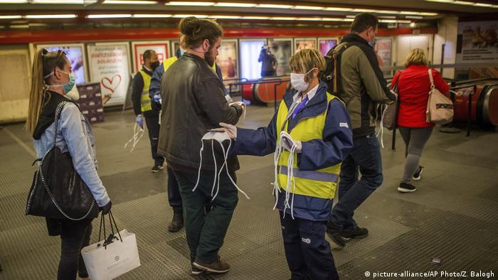 An employee working for the regional public transport company offers a face mask to a passenger at the Nyugati square in Budapest, Hungary, Monday, April 27, 2020. (picture-alliance/AP Photo/Z. Balogh)