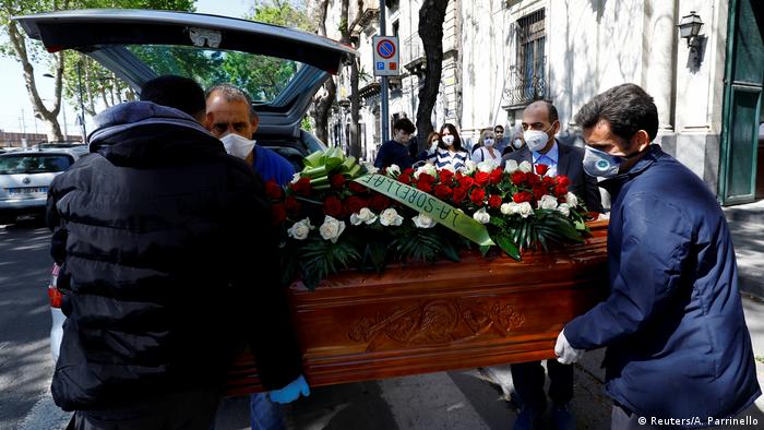 Pallbearers carry a coffin from a hearse while wearing face masks in Catalina, Italy. 