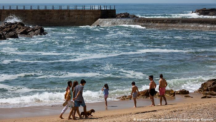 People take a stroll along a beach and play in the waves in Porto, Portugal on the first day of the lockdown being lifted.