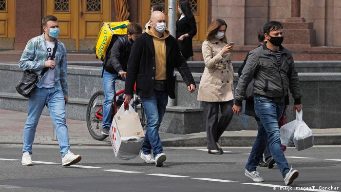 Fotoğrafta sokakta yürüyen maskeli insanlar görünüyor
