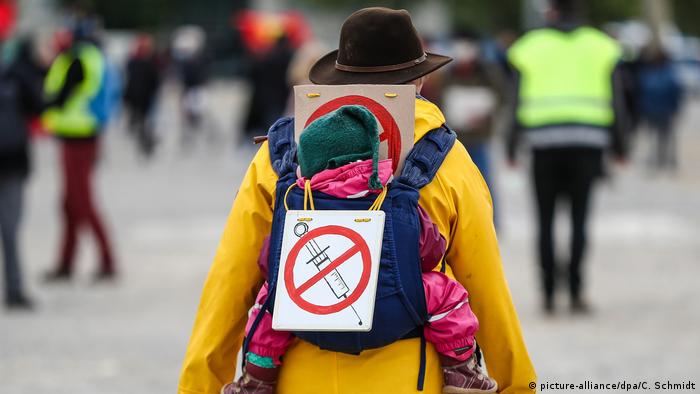 A man carrying a small child on his back, with an anti-vaccine sign