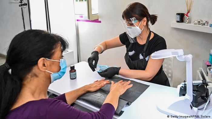 An employee wearing a face mask and shield (R) manucures a woman at a beauty saloon in Rome on May 18, 2020 during the country's lockdown aimed at curbing the spread of the COVID-19 infection, caused by the novel coronavirus. (Getty Images/AFP/A. Solaro)