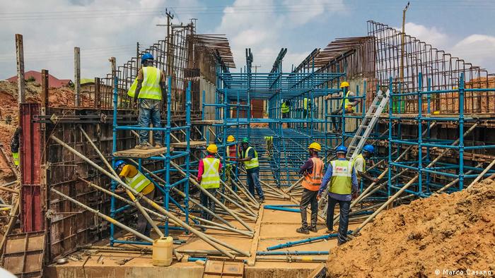 Construction workers in Kojokrom (Takoradi), Ghana, wearing hard hats and safety vests, work on scaffolding