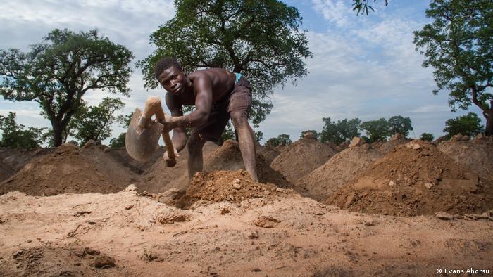 A man in Ghana digs earth mounds to dig for yams.