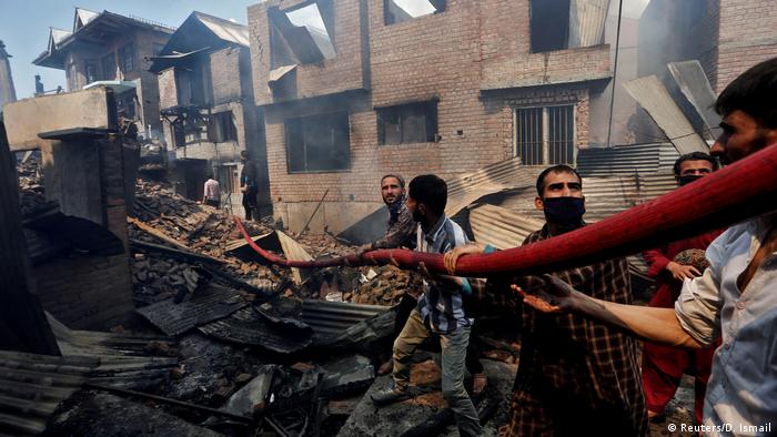 People hold a hosepipe amidst the smoldering debris of residential houses that, according to local media reports, were damaged during a gun battle between Indian security forces and suspected militants, in Srinagar May 19, 2020. (Reuters/D. Ismail)