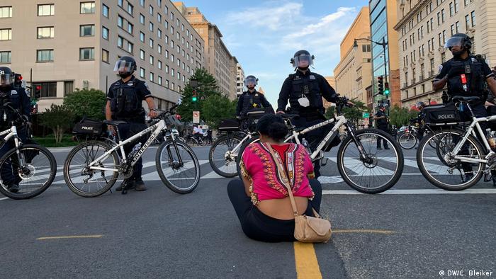 A young woman sits on the ground in front of police officers