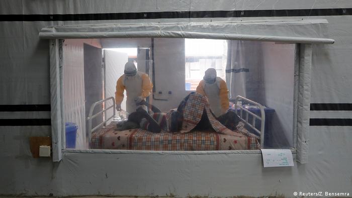 An Ebola patient lies in bed as two health workers examine him. (Reuters/Z. Bensemra)