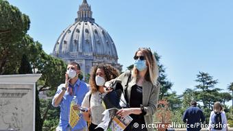 Туристы в масках на фоне купола собора Св. Петра в Ватикане