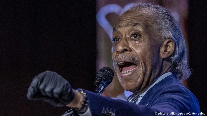 Al Sharpton speaking into a microphone with his left arm raised to shoulder height